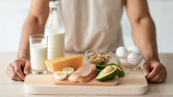 wooden-cutting-board-with-chicken-eggs-milk-avocado-and-nuts-with-mans-arms